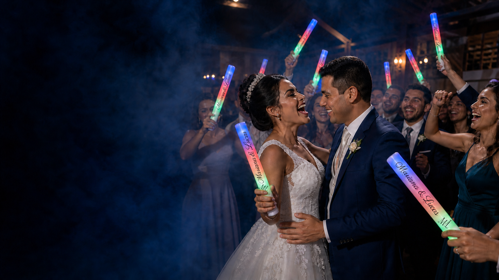 Noivos e convidados celebrando com bastões de LED personalizados para Mariana e Lucas em uma pista com fumaça
